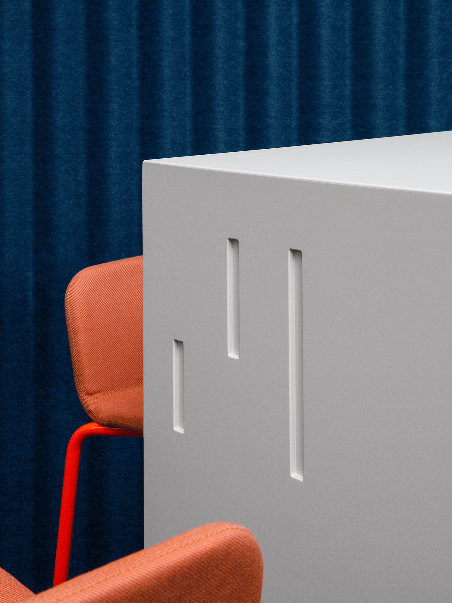 Prägung des KörberHaus-Logos in einen weißen Blocktisch. Zwei orangene Stühle und ein blauer Vorhang im Hintergrund sind zu sehen.