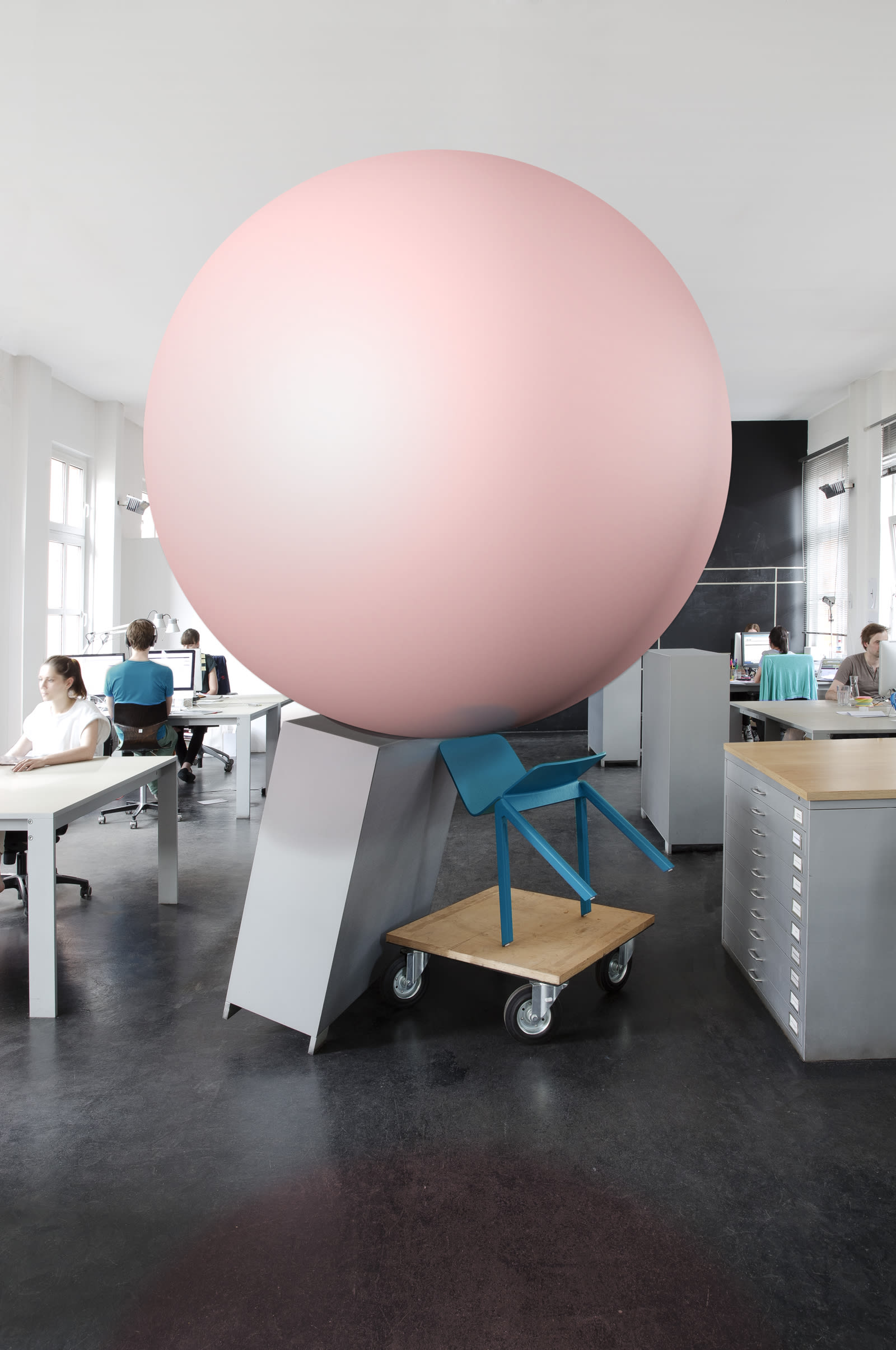 In the middle of the JUNO office, a giant pink ball is balanced on a rolling board, a blue chair and a shelf.