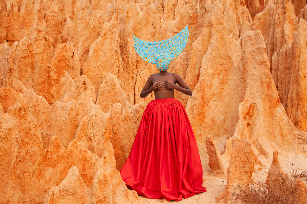 Woman with red skirt and blue headdress amid red rock