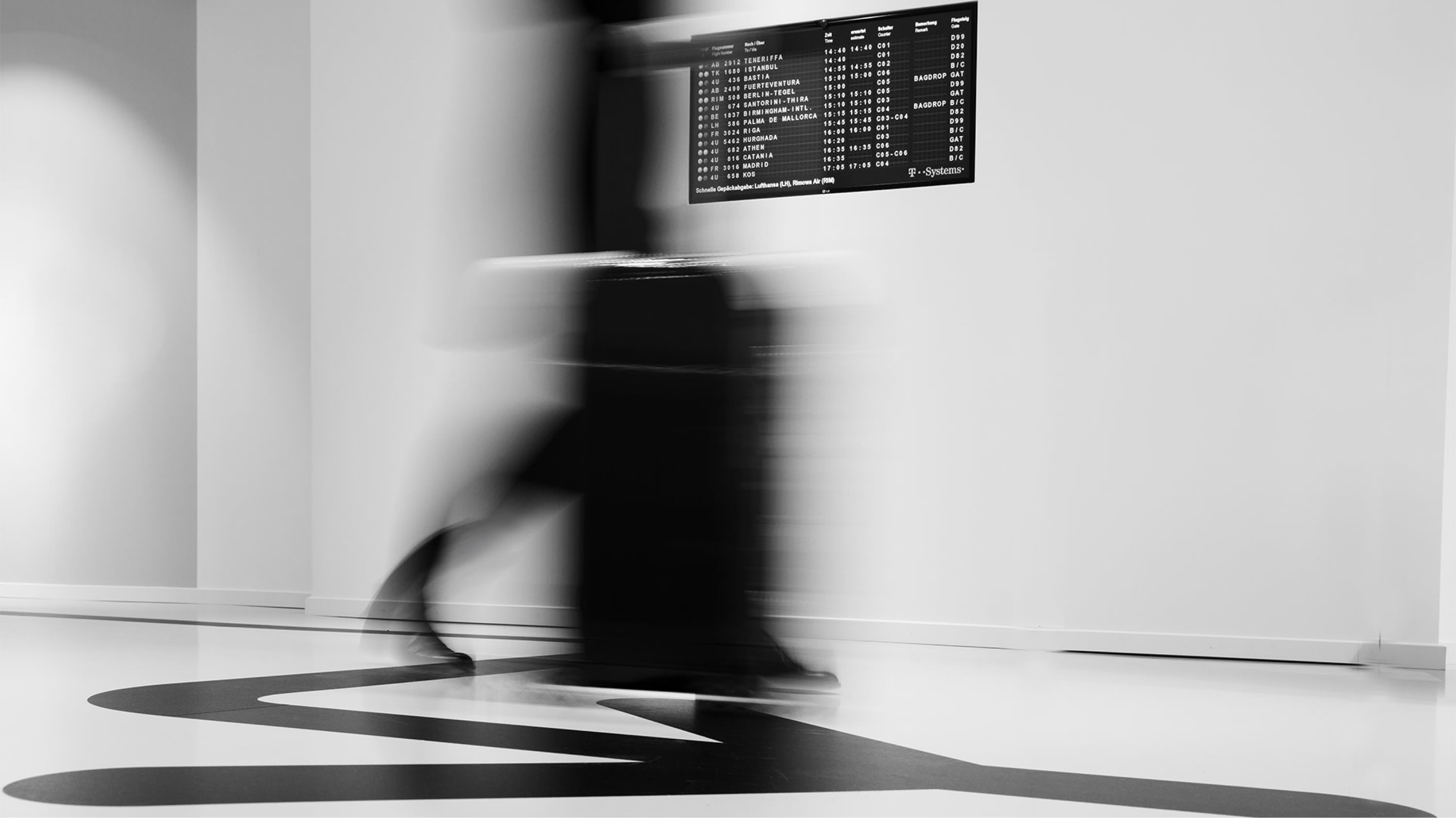 Kampagnenfotografie einer vorbeigehenden Person mit Koffer im Flughafen.