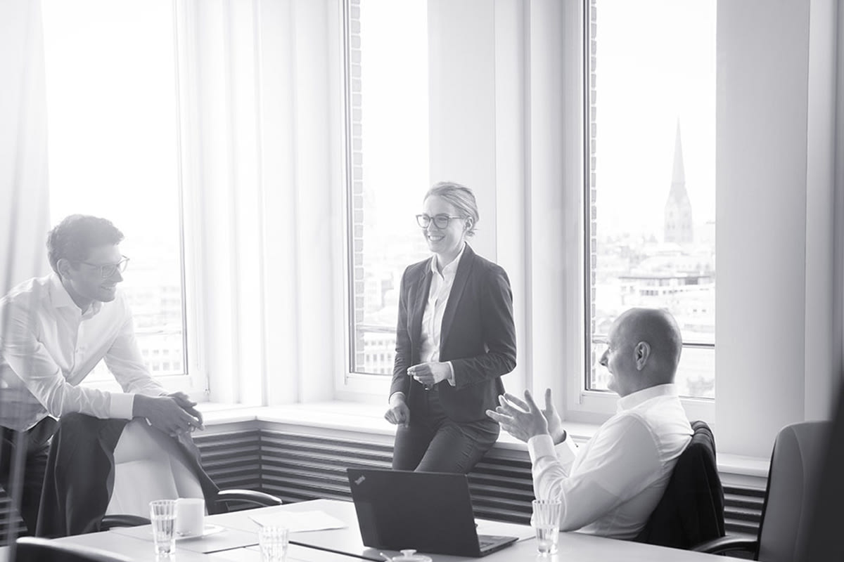 Three people in suits are talking in a conference room.