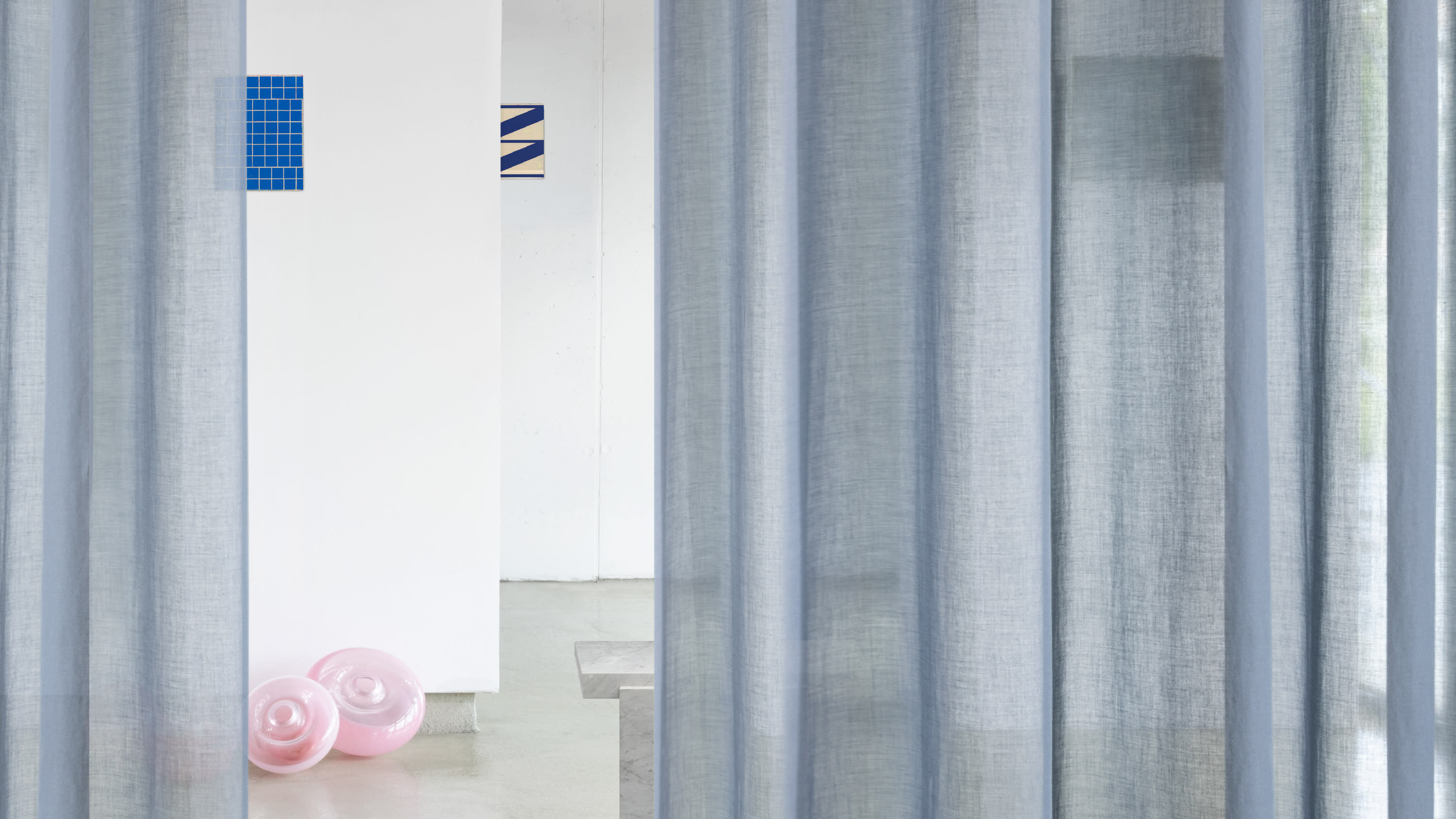 Campaign photography of a blue curtain. In the background is a room with more fabric samples on the wall.