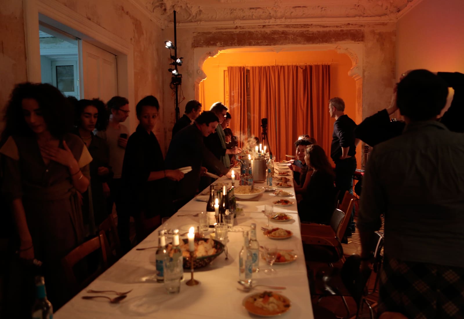 Dinner table in the M.Bassy rooms. Many people are standing around the table and talking.