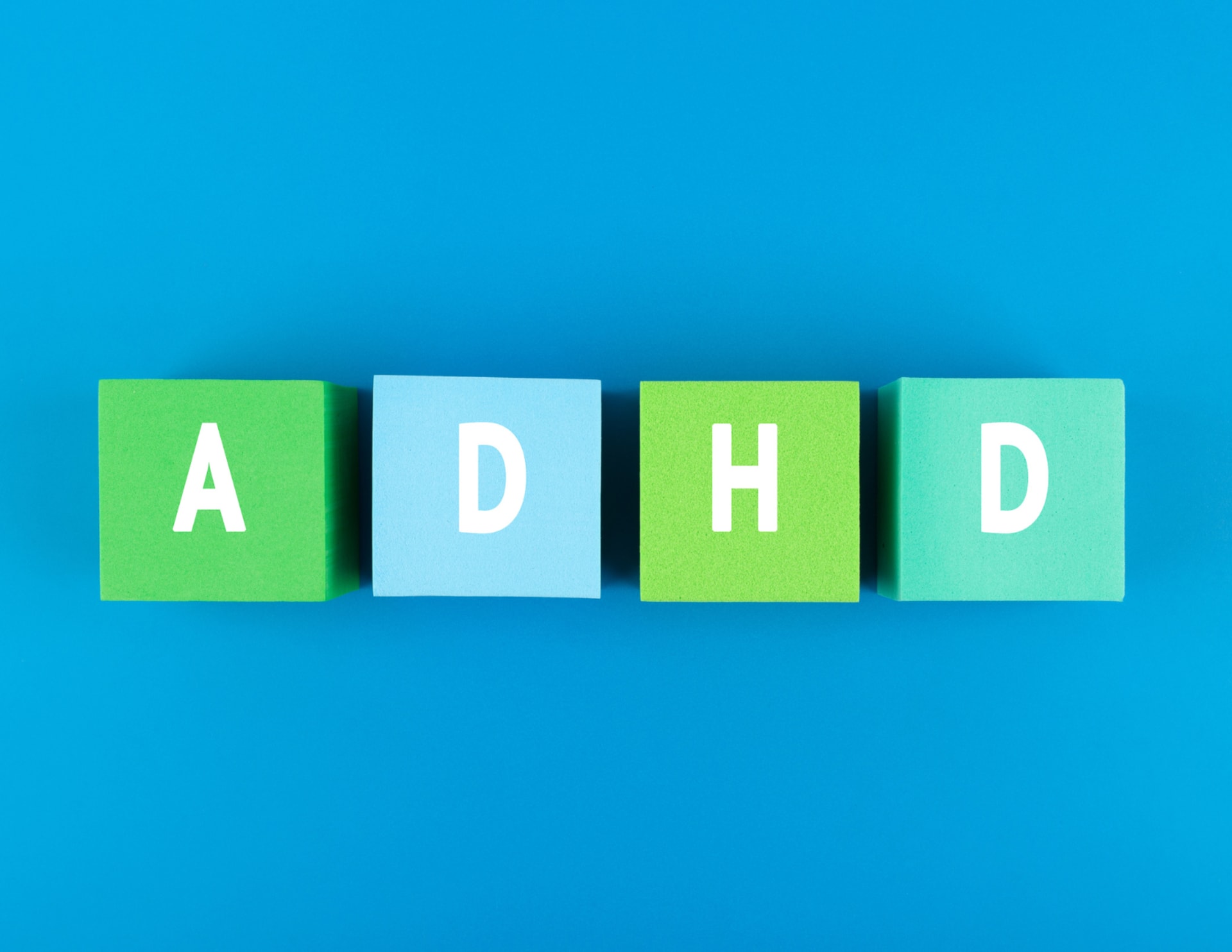 Four colored blocks on a blue background, each with a white letter spelling out "ADHD."