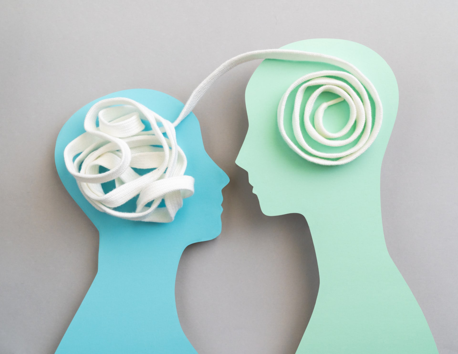 Two silhouette cutouts face each other; a tangled white cord is inside one head and a neatly coiled cord leads to the other.