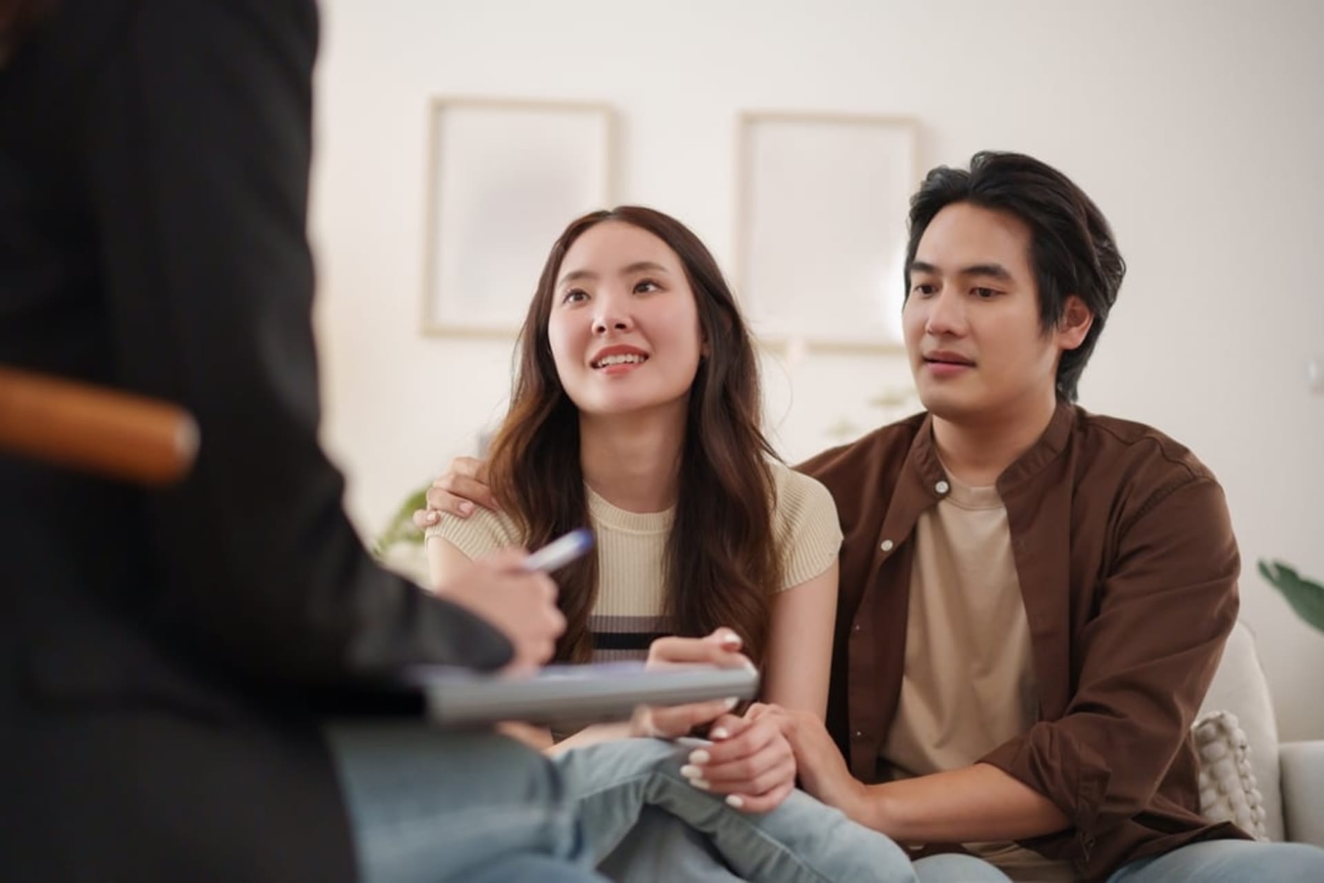 A couple sits close together, listening attentively to a pre marital counselor taking notes during a counseling session.