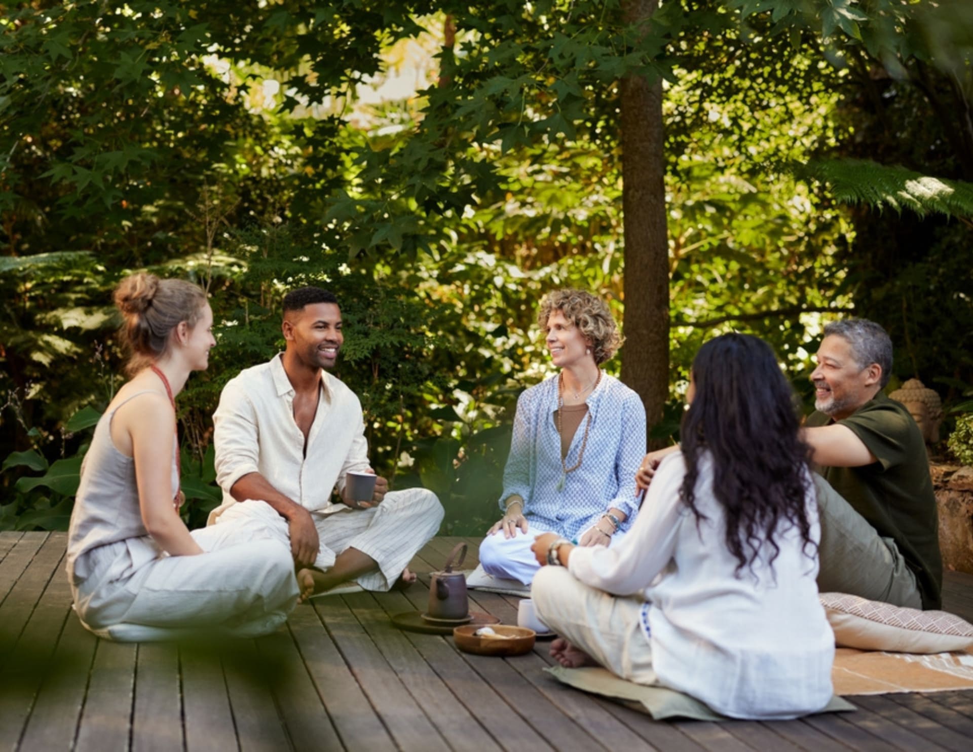 Five adults sit together on a wooden deck outdoors, engaged in conversation at a mental health retreat.