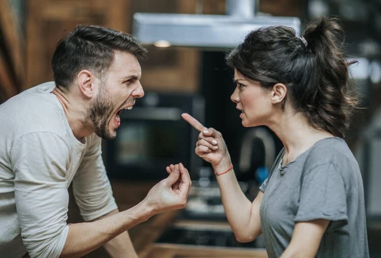 A man and a woman are in a heated argument in the kitchen of their Roseville home. The man is yelling with his mouth wide open, while the woman is pointing her finger at him. Both appear visibly upset, highlighting their need for Roseville therapy and counseling.