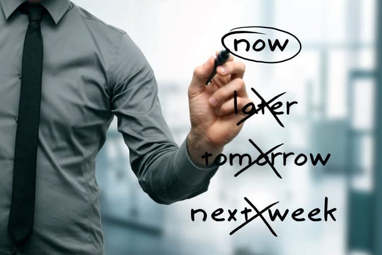 A person in a grey shirt, possibly seeking Roseville therapy and counseling, is using a marker to circle the word "now" while crossing out the words "later," "tomorrow," and "next week" on a transparent board.