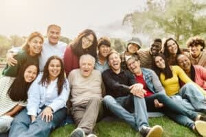 A diverse group of people of various ages sit closely together outdoors, smiling and laughing at the camera—capturing the spirit of connection that couples therapy and relationship therapists in San Francisco aim to foster.