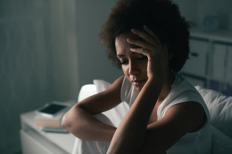 A person sitting indoors with a hand on their forehead, appearing contemplative or distressed, perhaps considering seeki