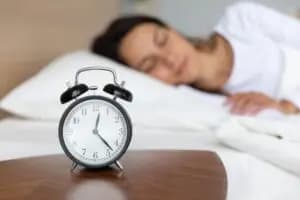 A person lying in bed with a clock in the background