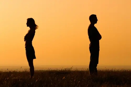 Silhouettes of a man and woman standing apart, facing away from each other in a field at sunset, depicting relationship stress.