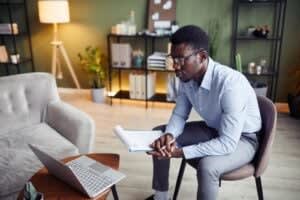 A therapist San Francisco, sitting on a chair holding a notebook and pen, looks intently at a laptop and doing online therapy in SF.