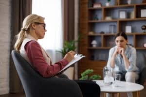 A therapist in San Francisco takes notes on a clipboard while speaking with a patient sitting across from her in a comfortable sf therapy office setting.