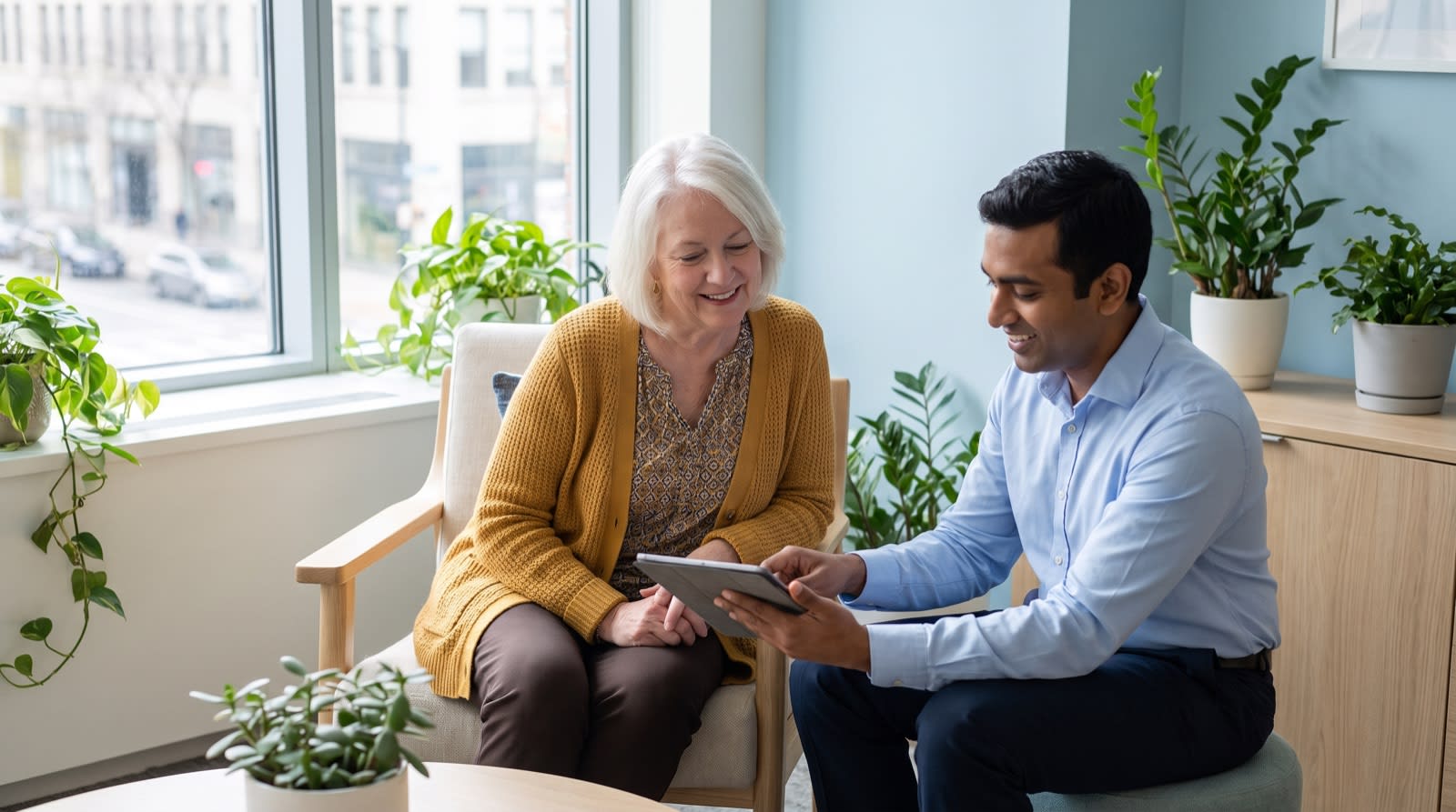 An older woman in a mustard cardigan talking easily with her cardiologist as they look at a tablet together.