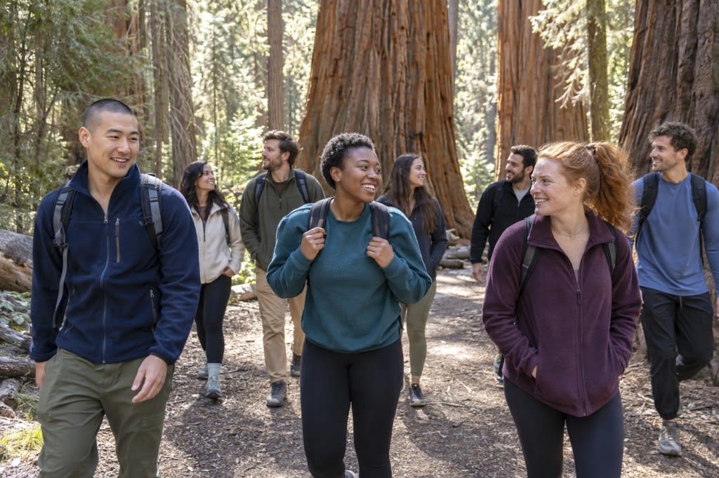 A diverse group of adults hikes and talks on a trail through a California redwood forest.