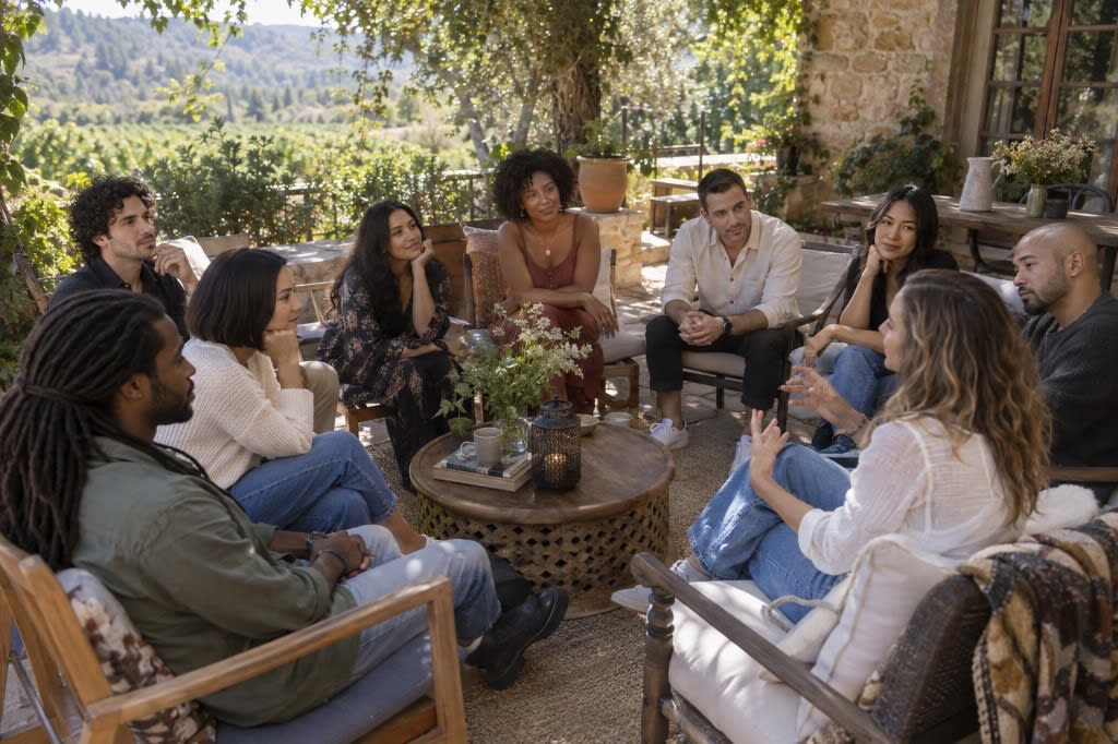 Adults sit in a circle on a vineyard patio during a group session, one woman speaking from the foreground.