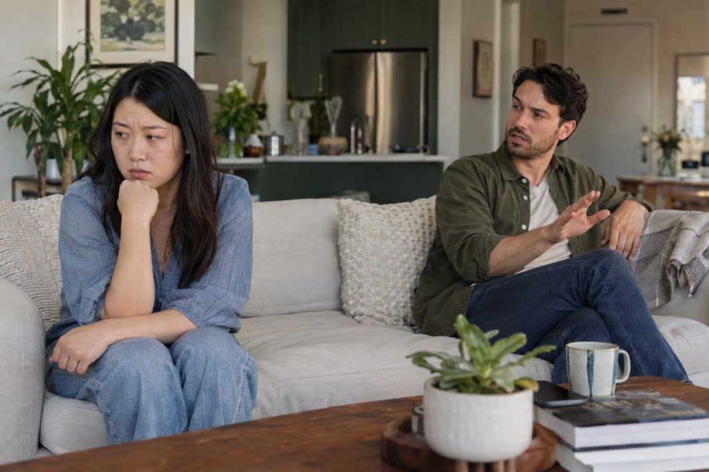 Tense interaction between partners seated apart in a living room.