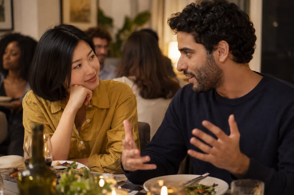 Two people at a dinner party absorbed in conversation, one listening closely as the other explains an idea