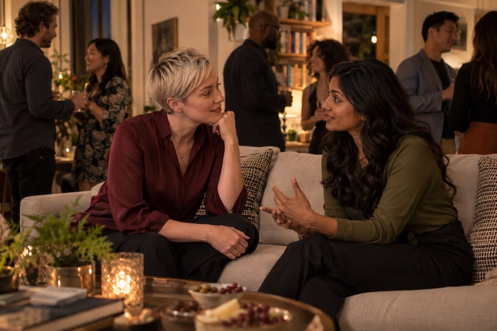 Two friends at a gathering leaning into a deep conversation while the rest of the party carries on behind them