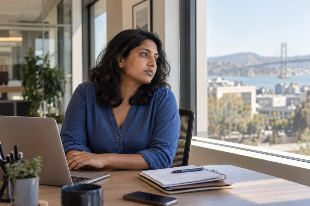 Woman at a San Francisco office desk looking out at the bay, showing workplace burnout and fatigue
