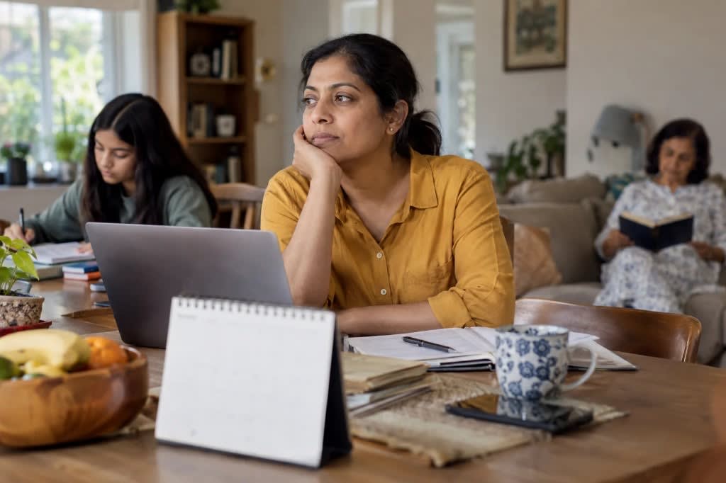 Woman at a kitchen table looking away while family members stay in the background, showing how perimenopausal depression can feel isolating