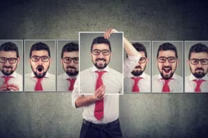 A man in a white shirt and red tie holds up a photo of himself smiling, surrounded by images of himself displaying various facial expressions—capturing the complexity of ADHD masking and the journey toward unmasking his true self.