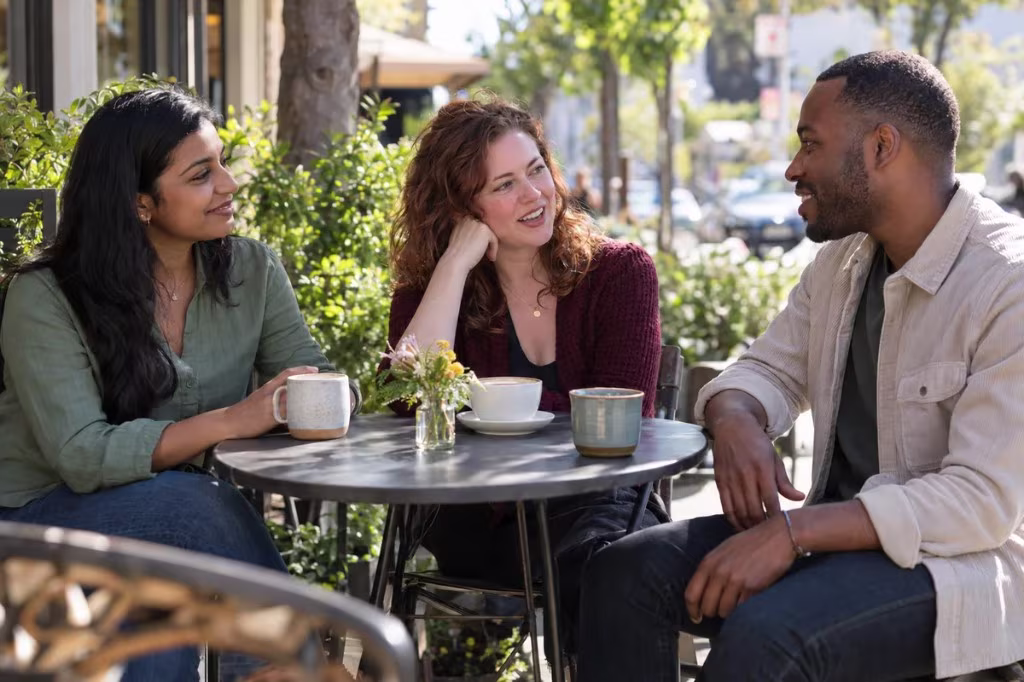 Three friends talk over coffee at an outdoor table, reconnecting face to face instead of only through a screen