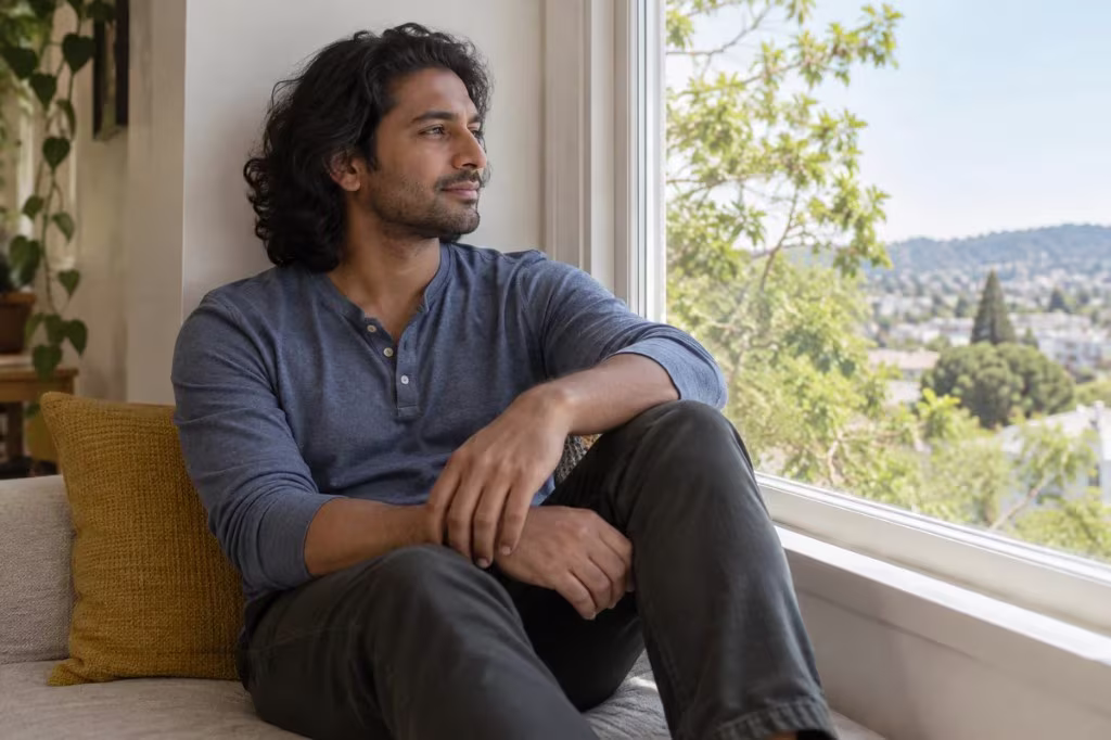 A man sits by a sunny window and looks out over a city, reflecting on when sexual attraction does and does not appear