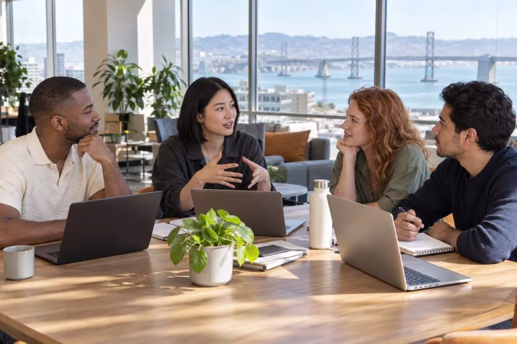 Four colleagues in a discussion around a conference table, with the Bay Bridge and the bay visible through the windows
