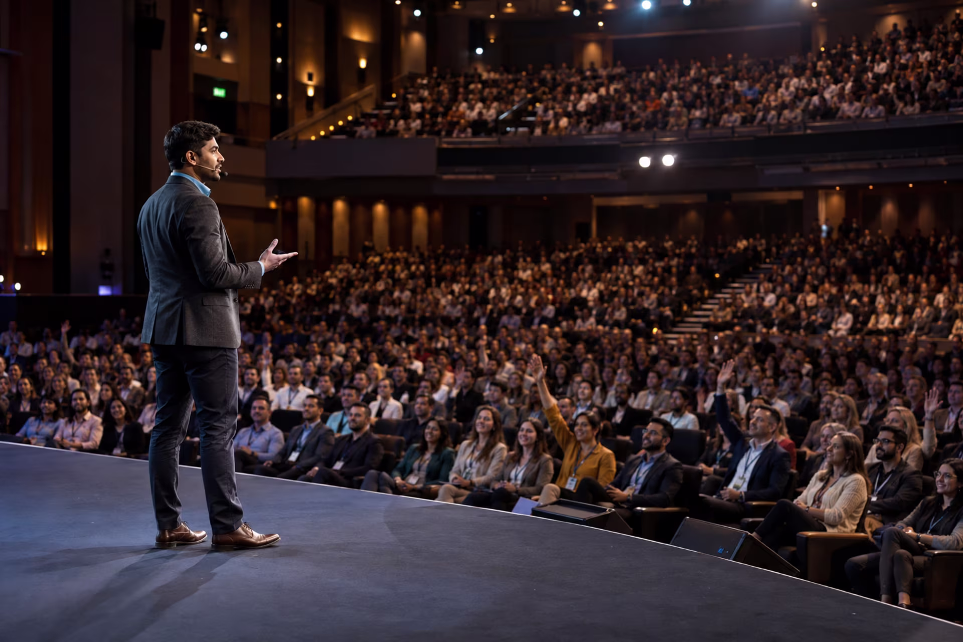 Public speaking in 2026: a speaker addresses a large auditorium audience with raised hands