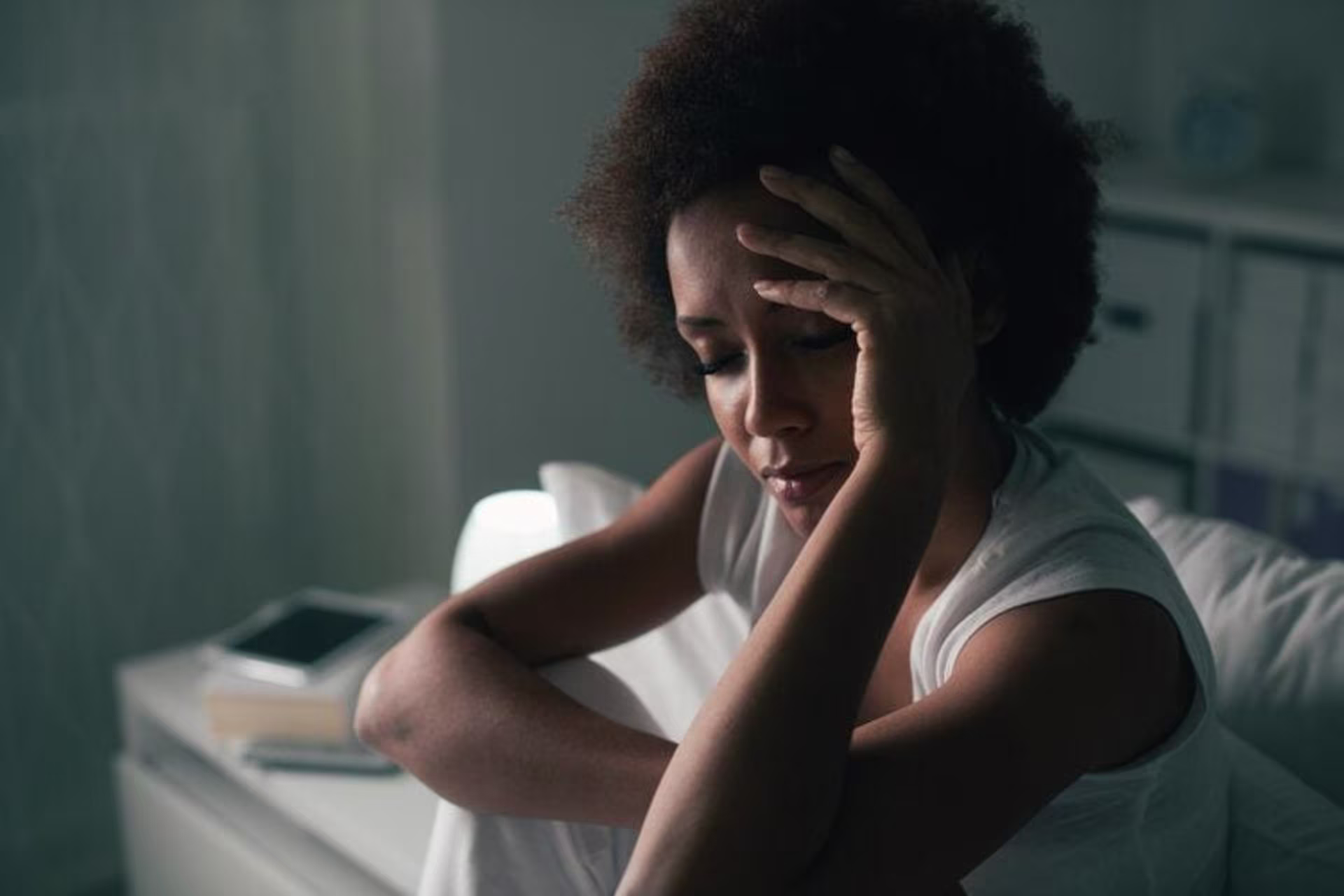 A person sitting indoors with a hand on their forehead, appearing contemplative or distressed, perhaps considering seeki