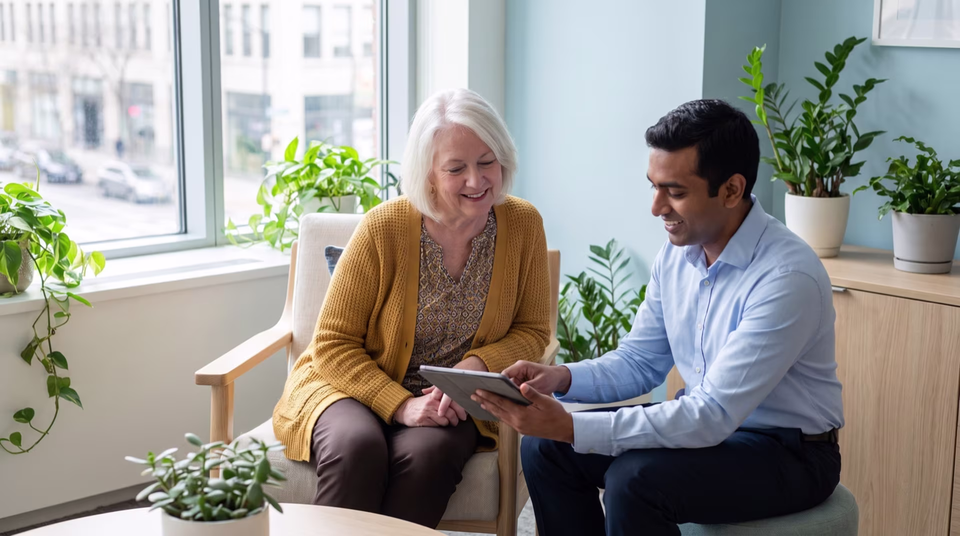 An older woman in a mustard cardigan talking easily with her cardiologist as they look at a tablet together.