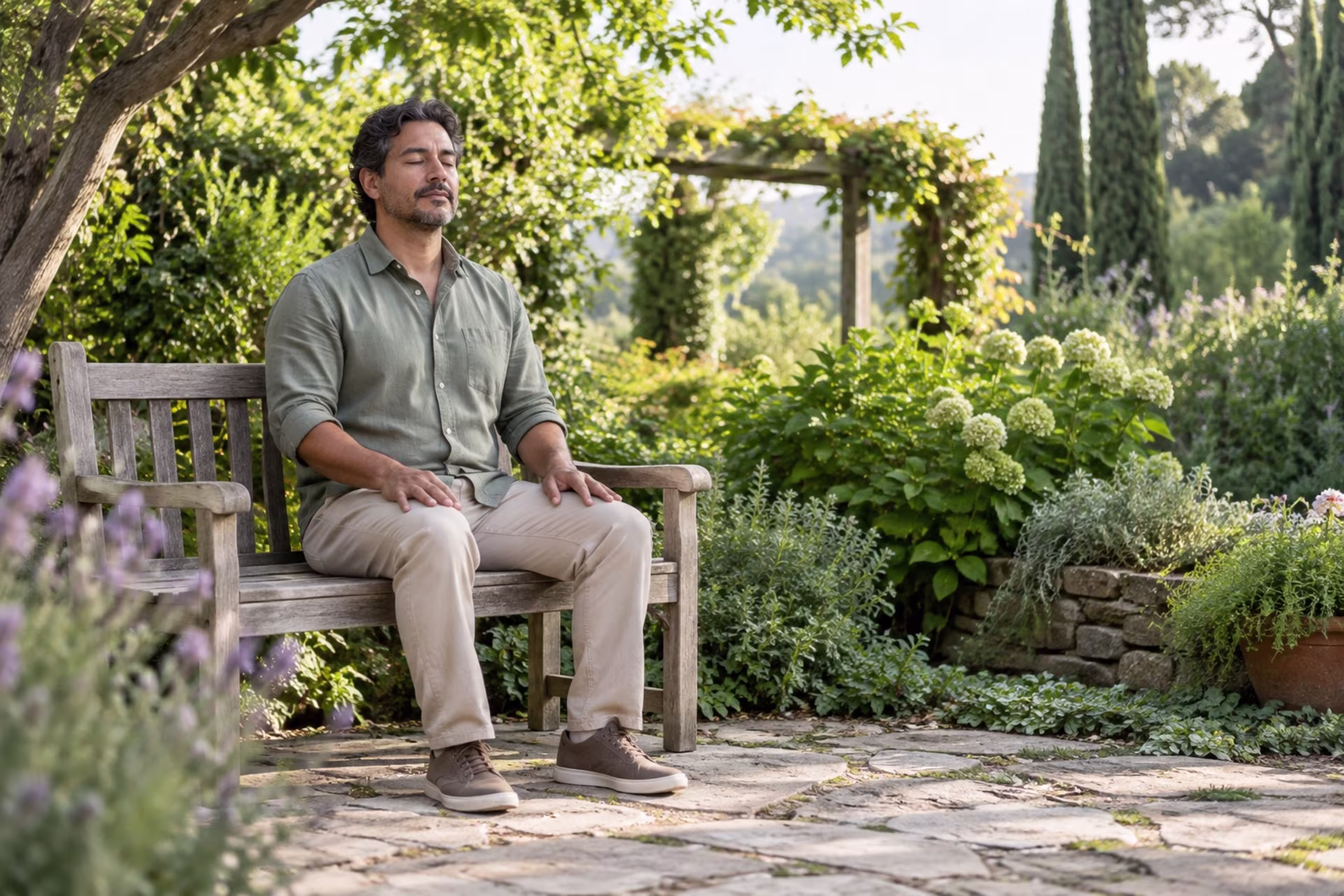 A man sits with eyes closed on a wooden garden bench, practicing a quiet mindfulness pause.