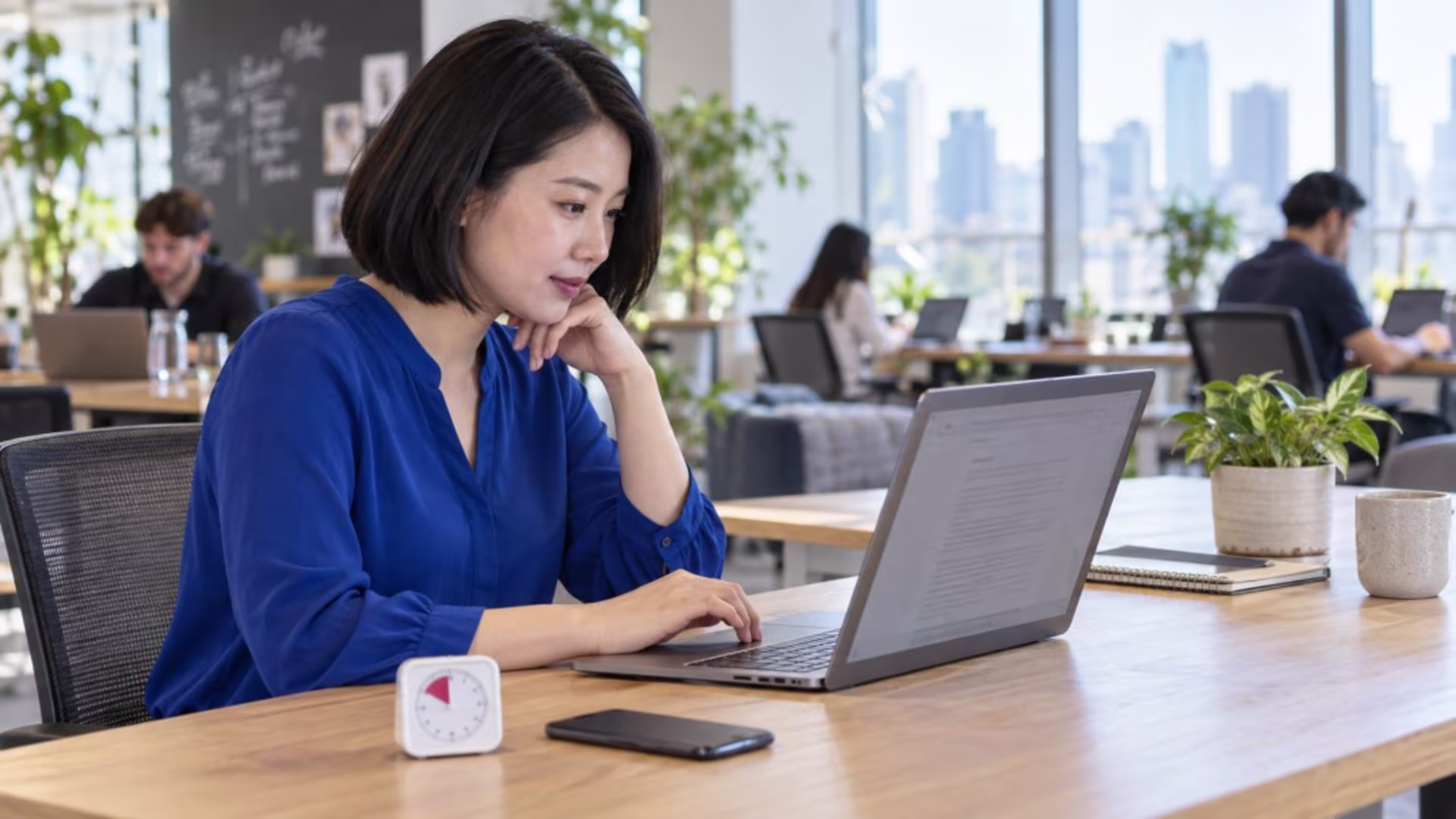 A person is seated at a desk, focused on a computer displaying a single document, while a timer is visible nearby, emphasizing their commitment to managing routine tasks and increasing productivity. This setup highlights the importance of staying focused and organizing tasks effectively to accomplish high impact work.