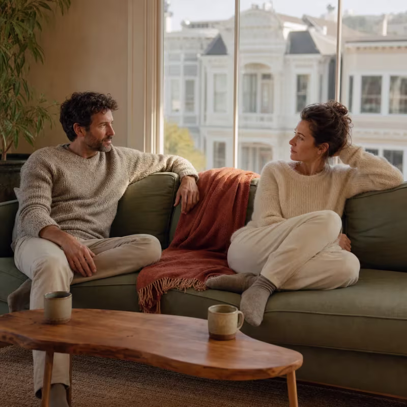 Couple sitting on a sofa in a sunlit San Francisco apartment talking honestly about their marriage during discernment counseling in San Francisco, CA — San Francisco discernment counseling near me
