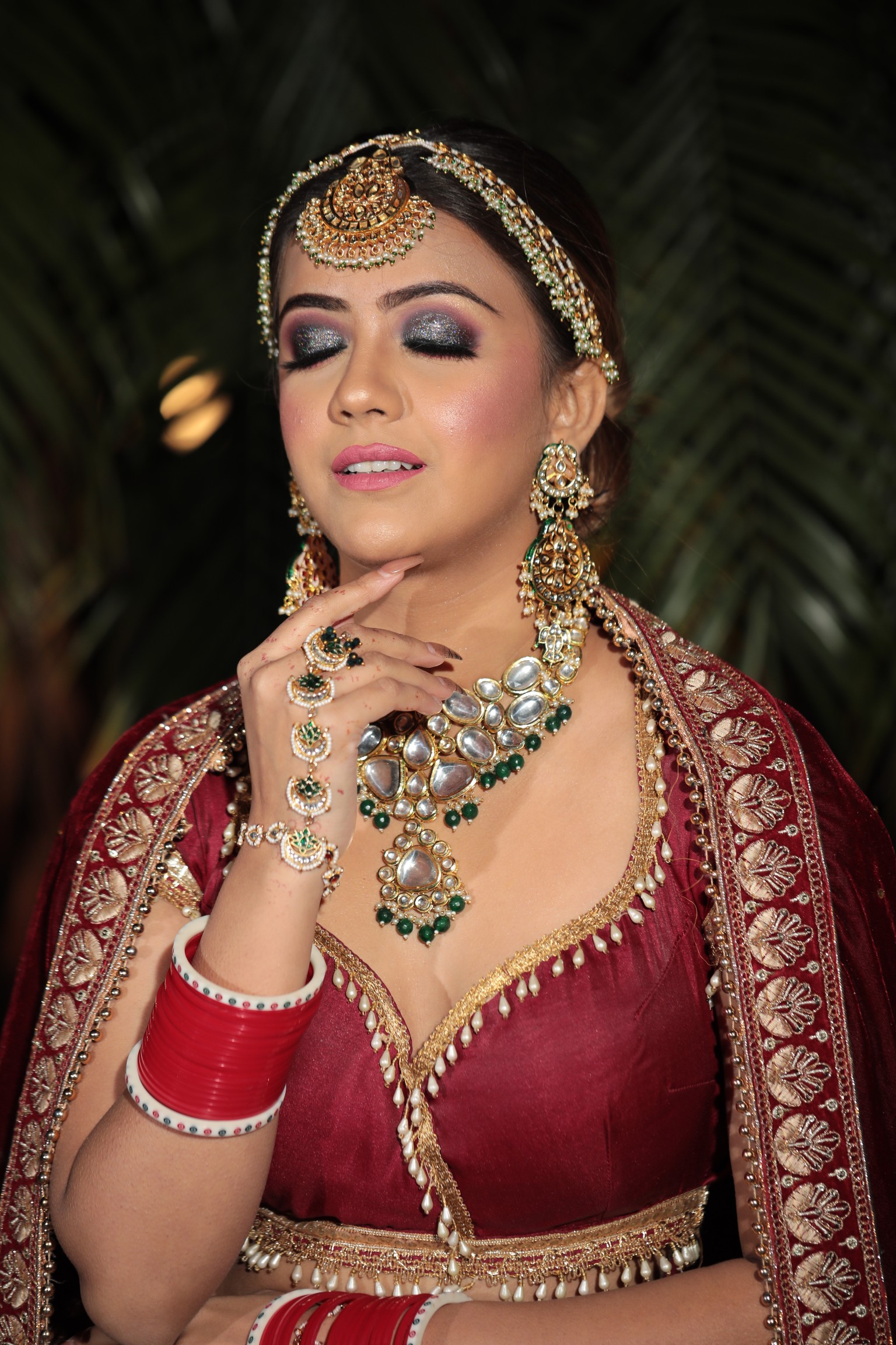 Indian bridal makeup with sparkling eyes, traditional jewelry, and red lehenga.