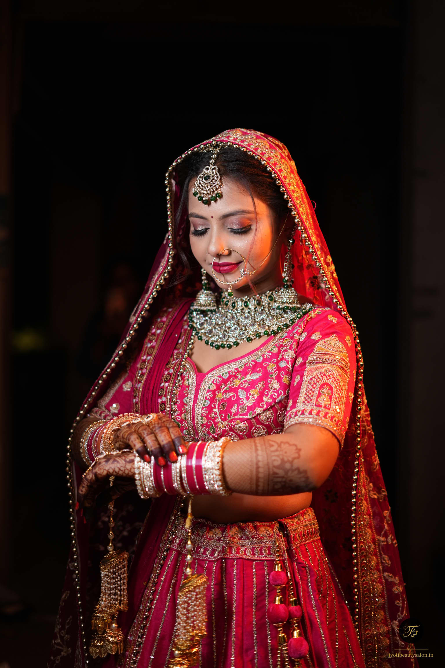 Indian bride in magenta lehenga adjusting her chooda and gold kaleere at Jyoti Beauty Salon in Chapra.