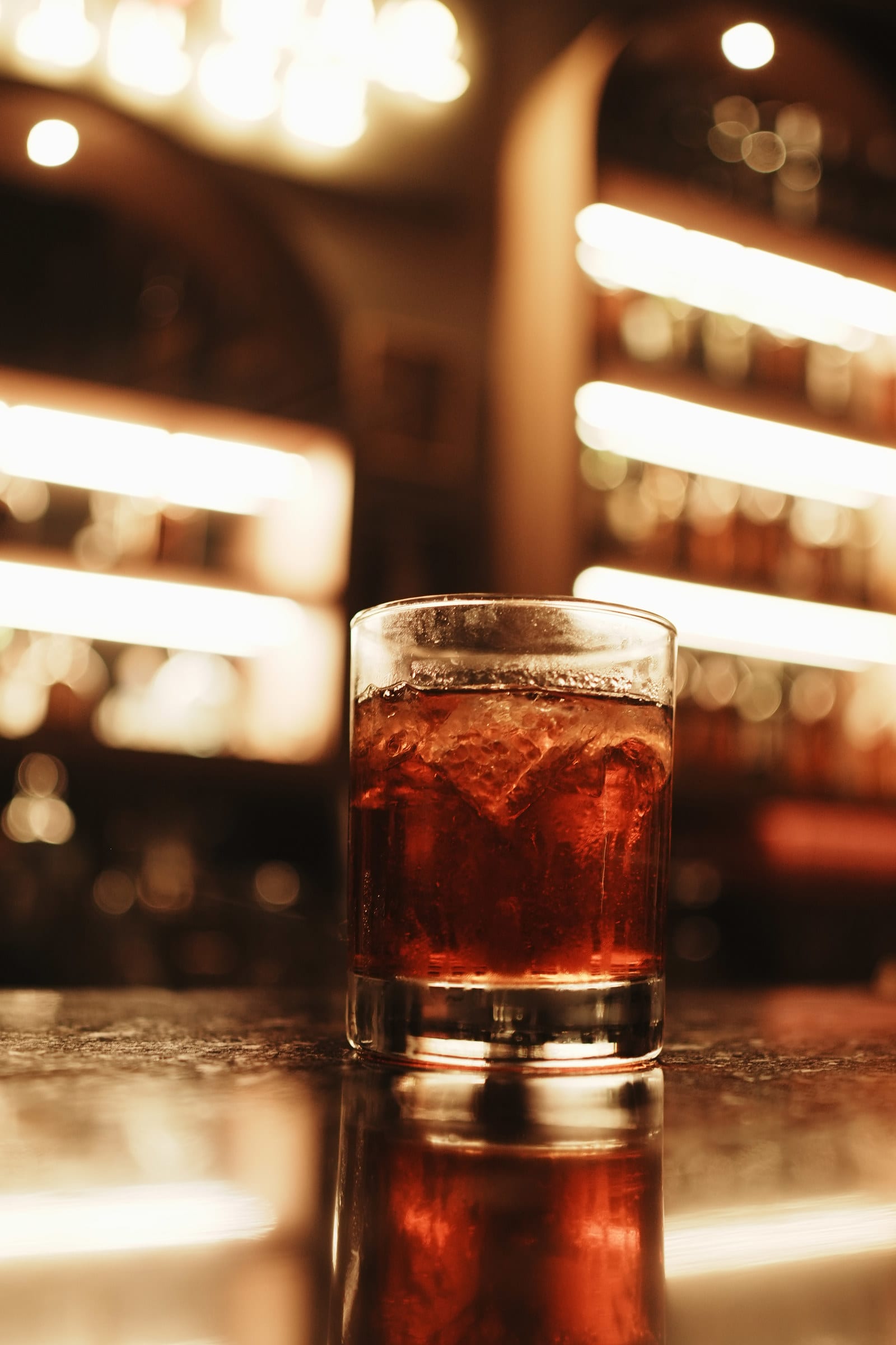 Dark red drink on ice in front of glowing bar shelves