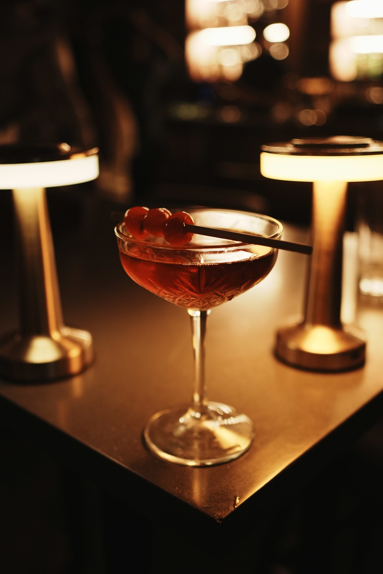 Cocktail with cherries between two glowing table lamps