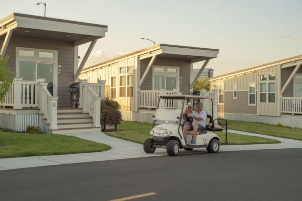 A couple driving a golf cart past some cottages.