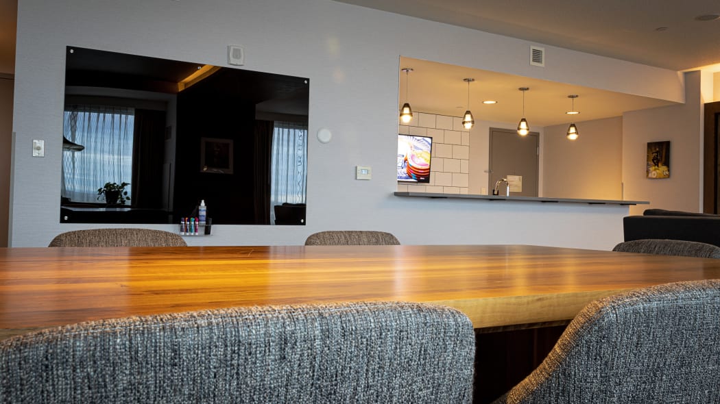 a view of a large wall mounted TV and the kitchen area from chairs at the table