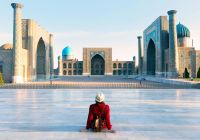 Tourist woman with hat and dress red sitting on registan an old public square uzbekistan