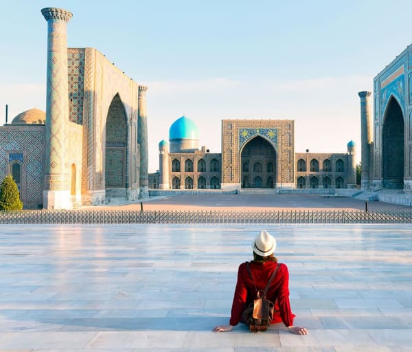 Tourist woman with hat and dress red sitting on registan an old public square uzbekistan