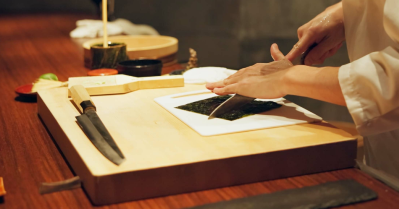 Japan chef, restaurant and cutting seaweed for sushi, glasses and precision with knife for raw fish