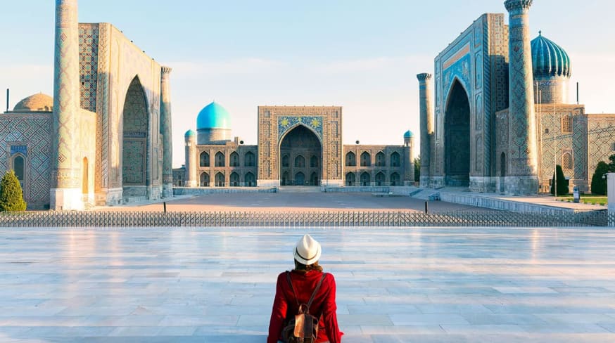Tourist woman with hat and dress red sitting on registan an old public square uzbekistan