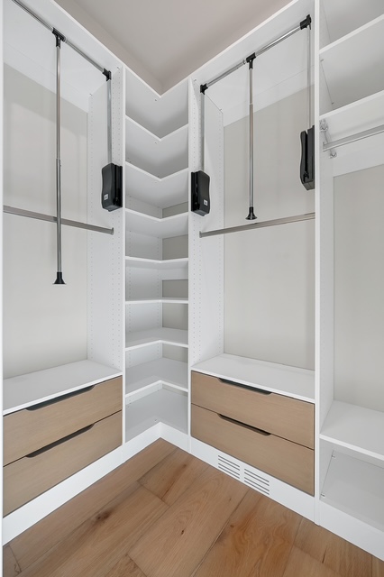 Corner custom closet with built-in drawers, angled shelving, and pull-down hanging rods in Green Bay, WI.