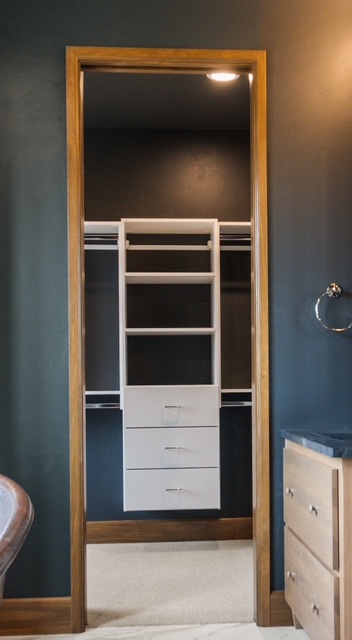 Custom reach-in closet with built-in drawers, shelving, and hanging rods viewed through bathroom doorway in Green Bay, WI.