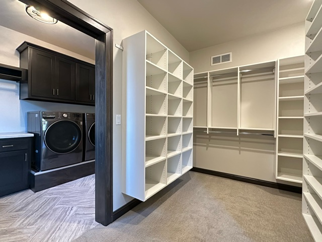Custom closet with open shelving, hanging rods, and direct access to adjacent laundry room in Green Bay, WI.
